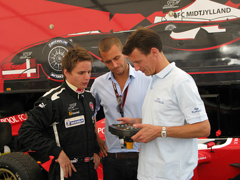FC Midtjyllands Superleague Formula-kører Kasper Andersen (tv) forklarer Hans Kongelige Højhed Prins Joachim om finesserne i racerens højteknologiske rat. I midten Alex Chambers, Sponsorship Manager, Superleague Formula.